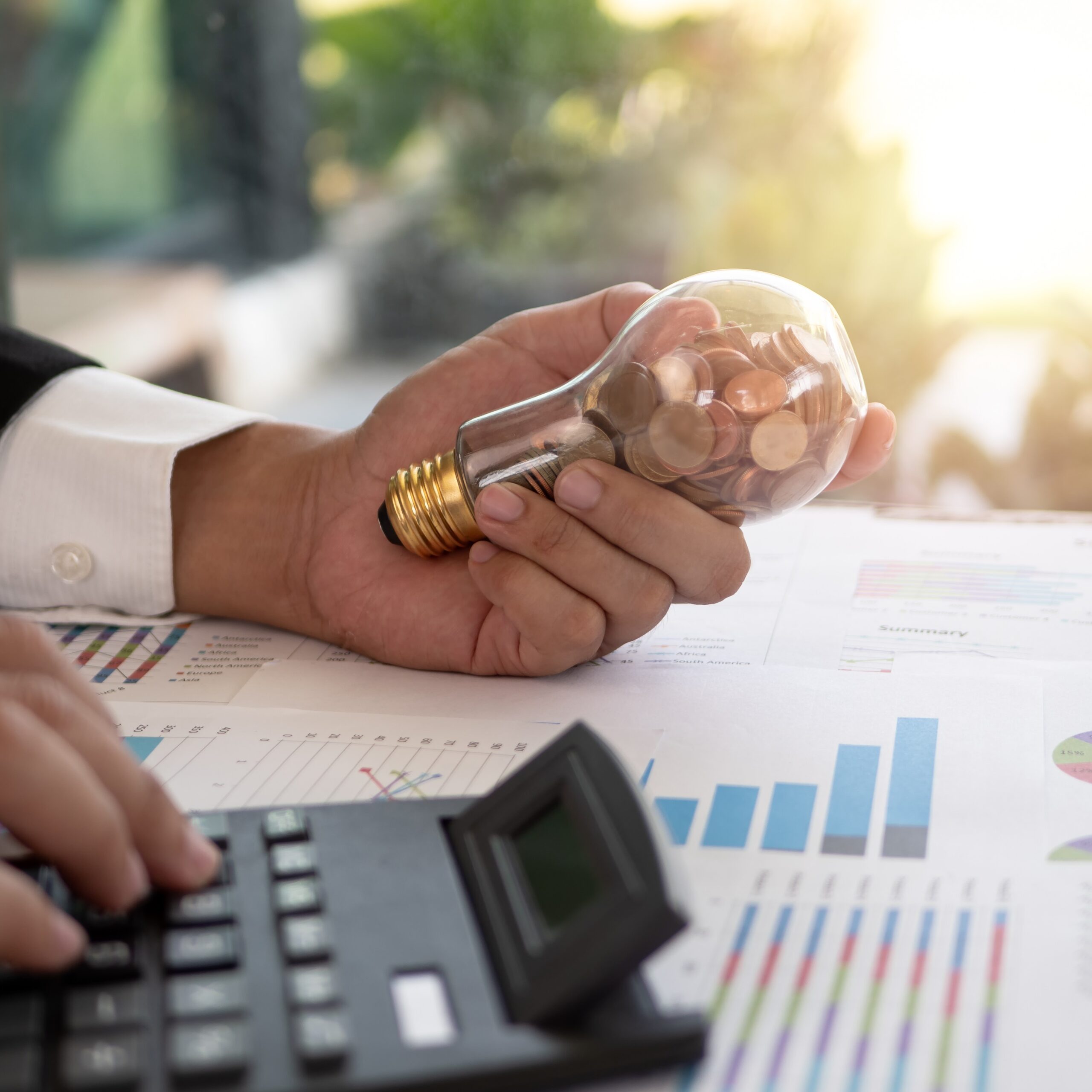 Mano de un empresario sosteniendo una bombilla con una moneda. Concepto de reducción de costes y consumo energético.