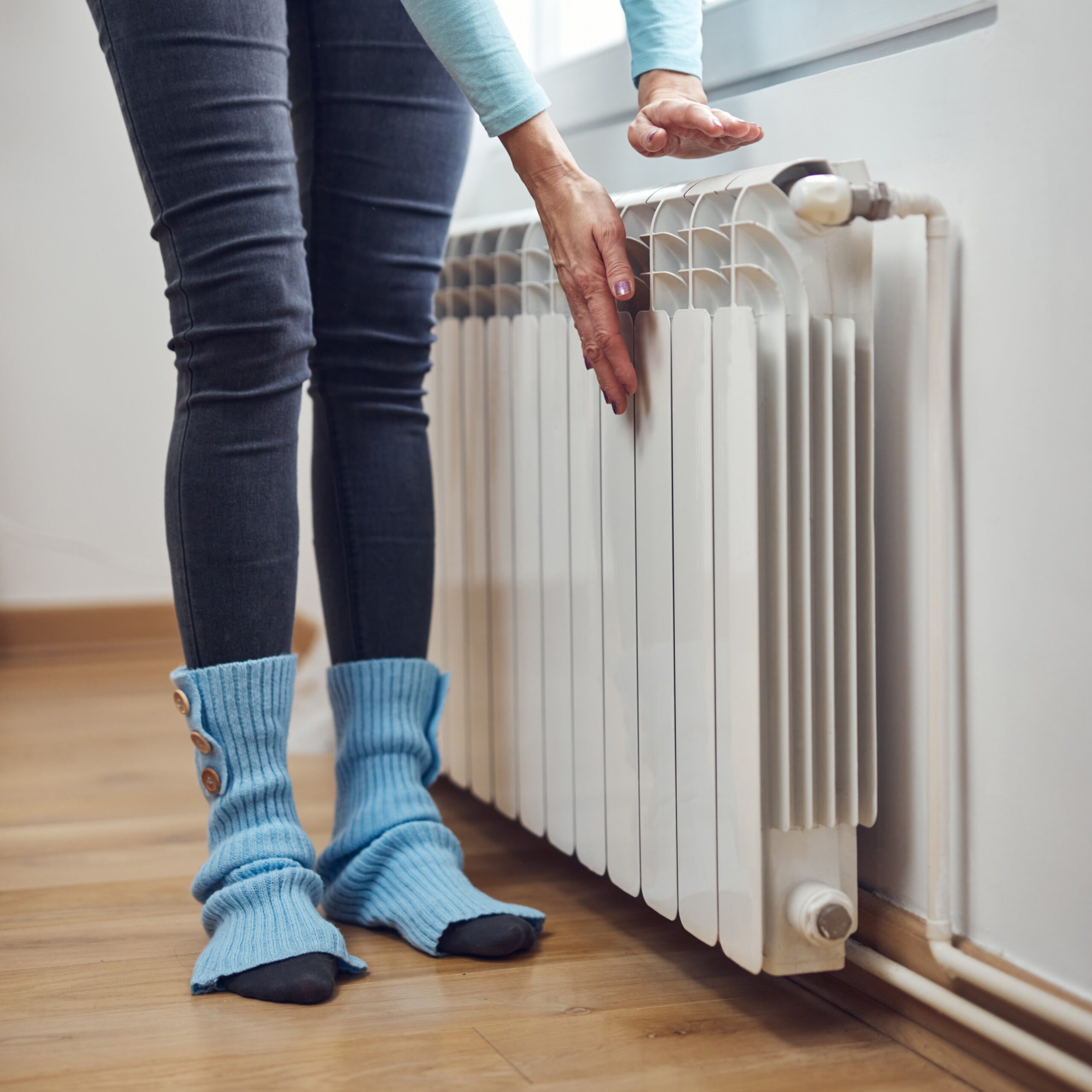 Mujer calentándose las manos en el radiador durante los fríos días de invierno.