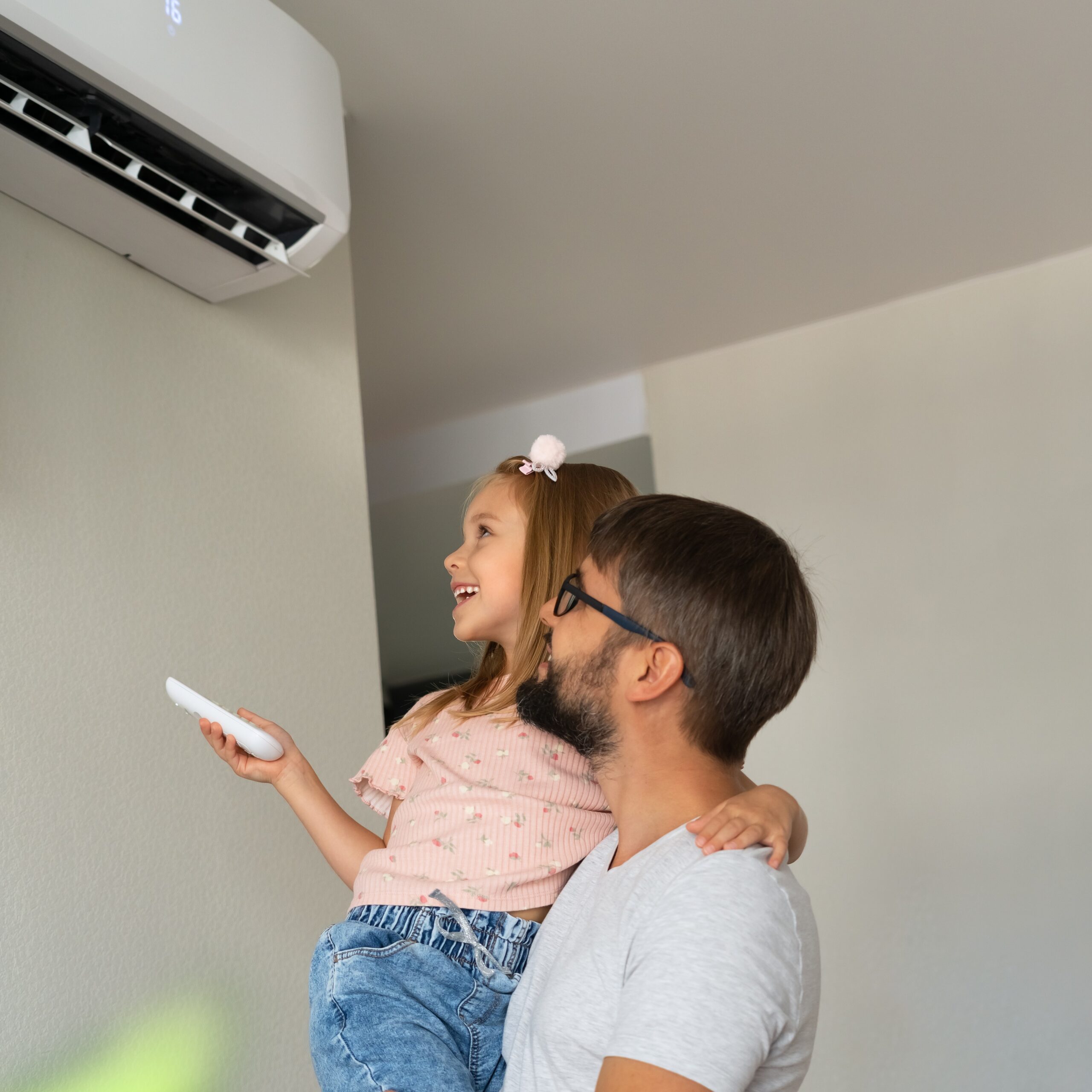 Familia feliz: padre e hija pequeña se divierten encendiendo el aire acondicionado con el control remoto. Sistema de refrigeración.