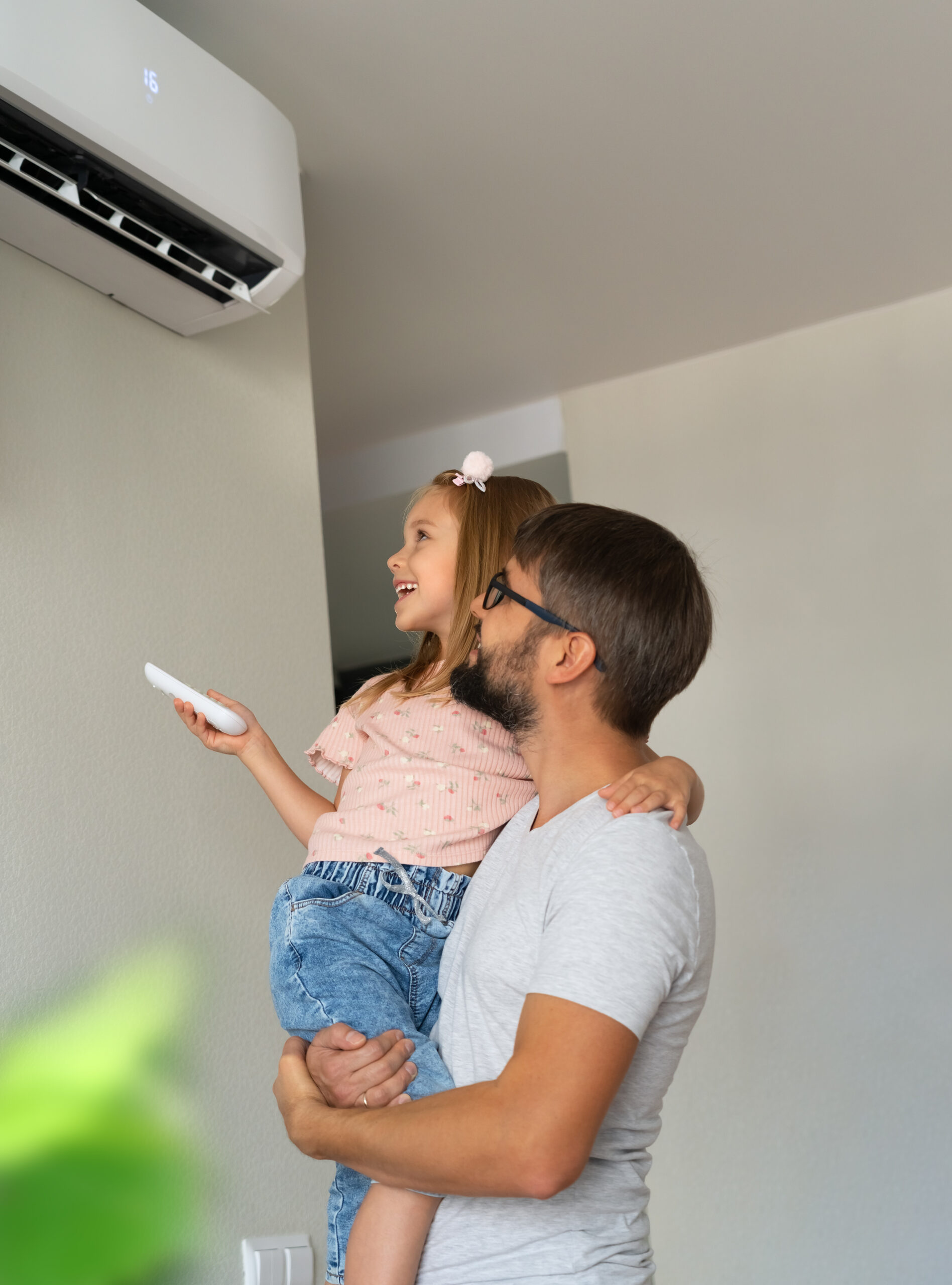 Familia feliz: padre e hija pequeña se divierten encendiendo el aire acondicionado con el control remoto. Sistema de refrigeración.